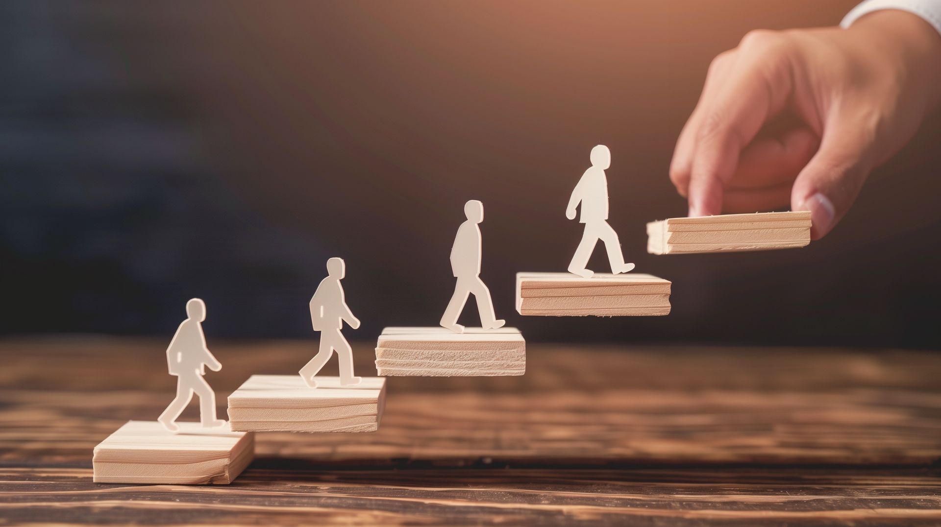 Hand placing wooden block for person silhouette climbing stairs, symbolizing career or personal growth.