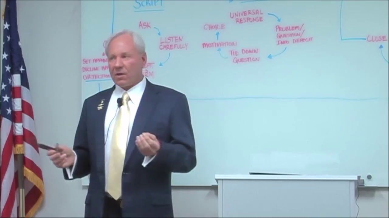 Man in suit gesturing at a whiteboard with a circular diagram; American flag in the background.