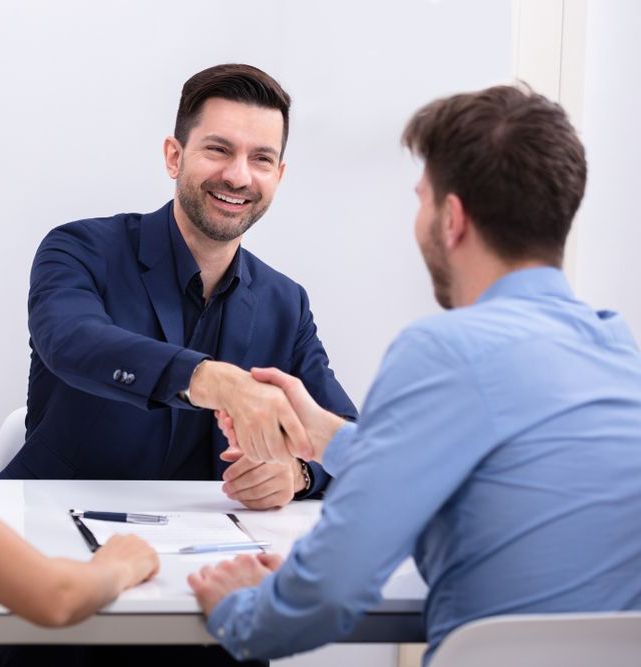 A Man In A Suit Is Shaking Hands With Another Man — Charlestown Law Firm In Sydney, NSW