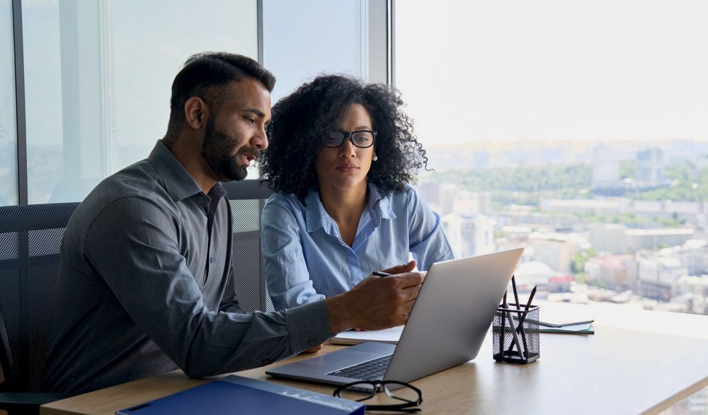 A Man And A Woman Are Sitting At A Desk Looking At A Laptop Computer — Charlestown Law Firm In Charlestown, NSW