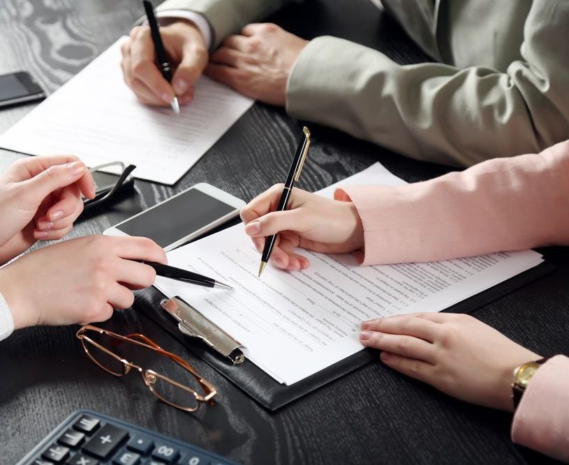 A Group Of People Are Sitting At A Table Writing On Papers — Charlestown Law Firm In Charlestown, NSW
