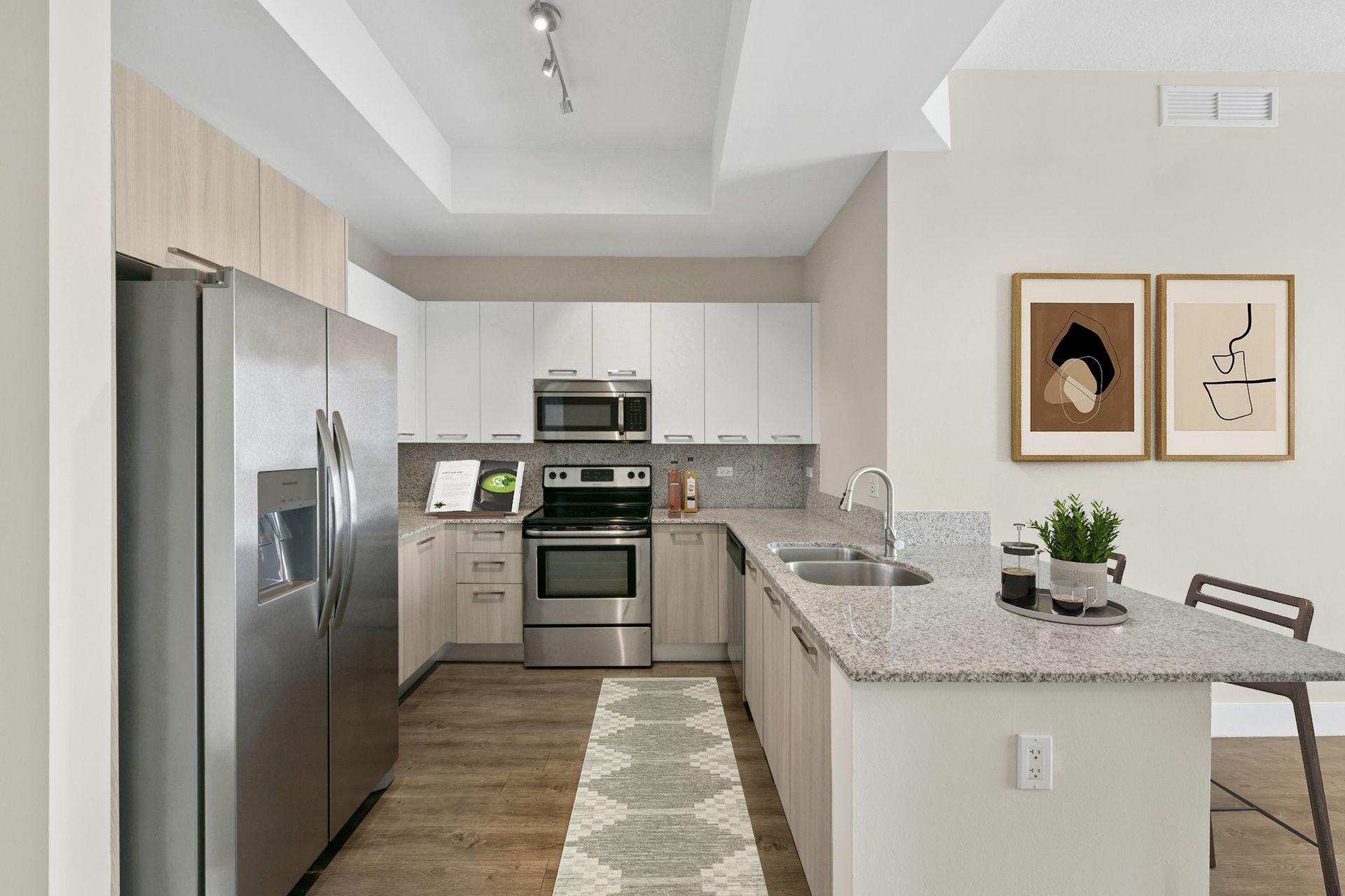 Modern kitchen with stainless steel appliances, white cabinets, a breakfast bar, and framed wall art.
