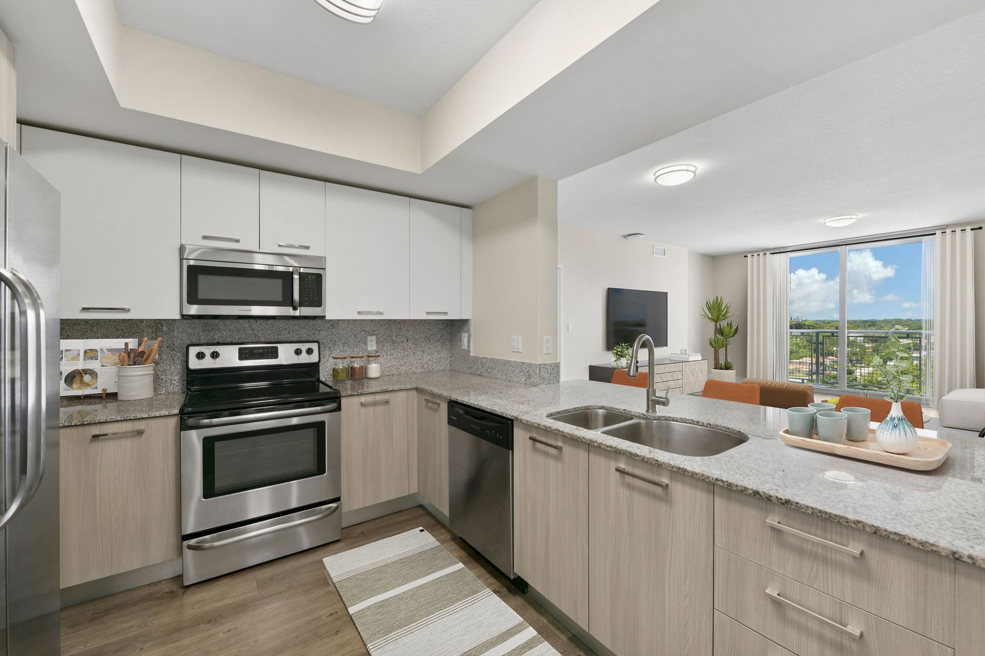 Bright modern kitchen with stainless appliances, light wood cabinets, and a breakfast bar facing a sunny living area.