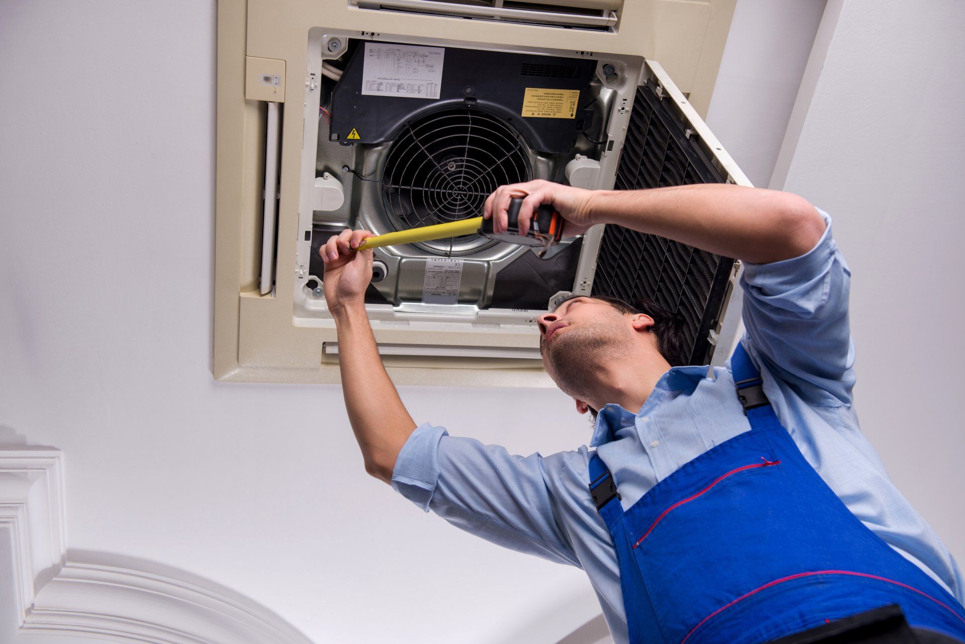 Young repairman repairing ceiling air conditioning unit