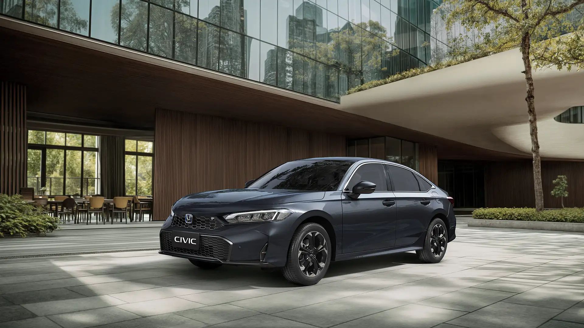 Dark sedan parked in front of a modern glass building with trees and a courtyard