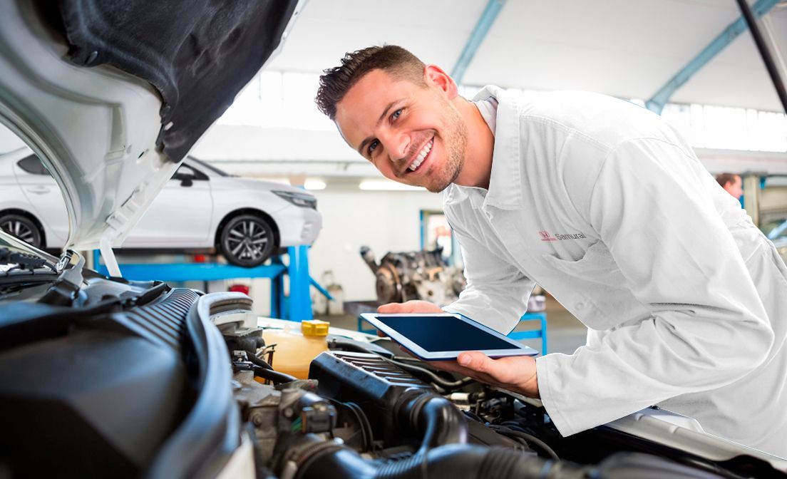 Mechanic smiling while inspecting a car engine in an auto repair shop