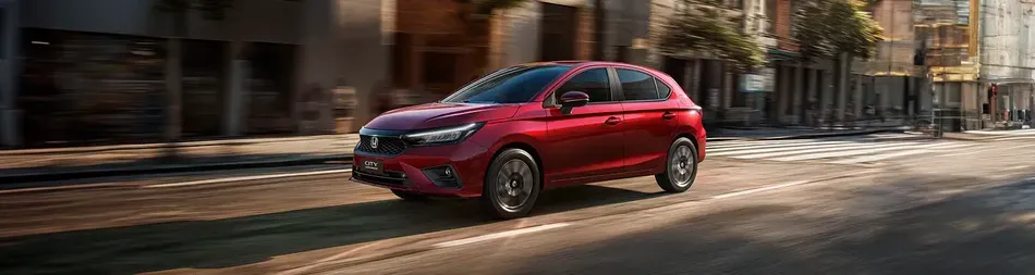 Red compact car driving on a city street with motion blur in the background