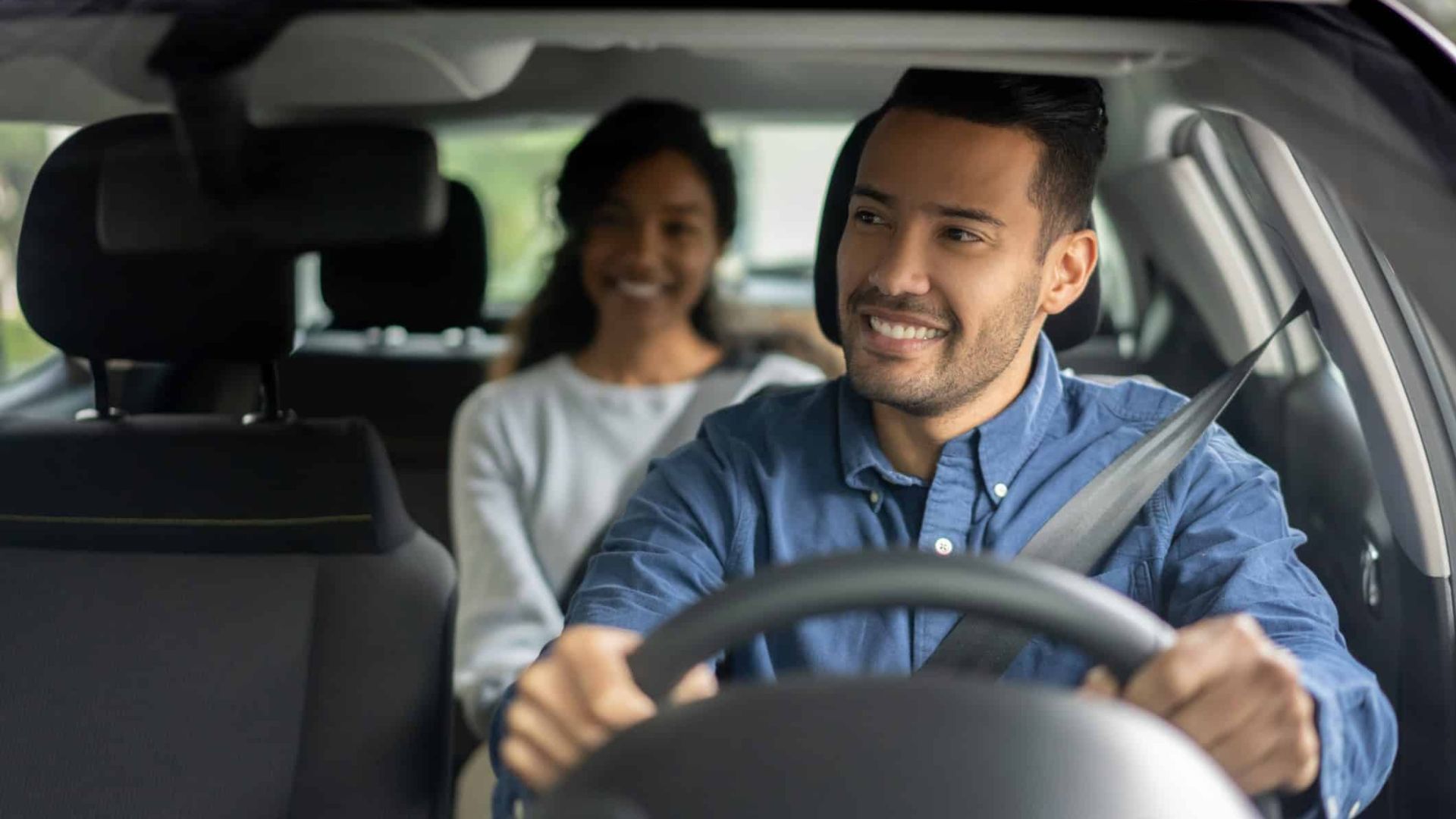 Smiling driver and passenger in a car, seen from the front seat.