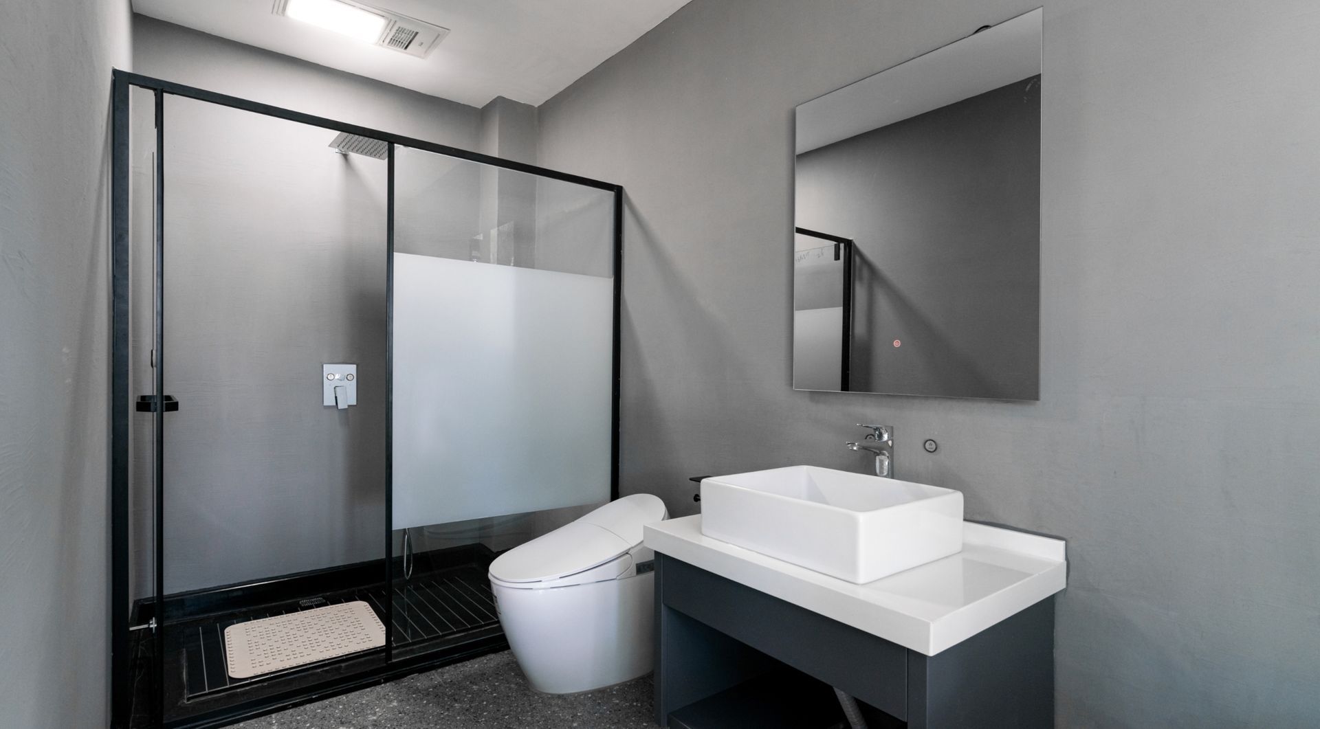 Modern gray bathroom with glass shower, toilet, and white sink vanity
