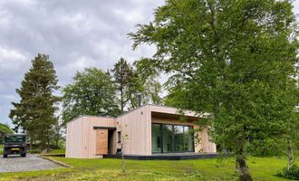 Modern wooden cabin with large glass windows in a green wooded setting