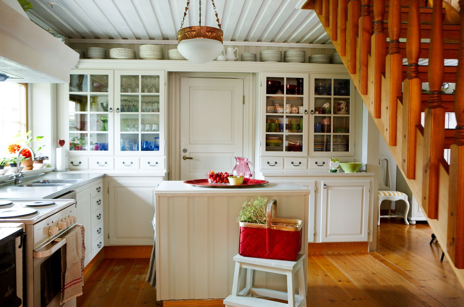 Bright white kitchen with wooden floors, central island, and staircase under a slanted ceiling