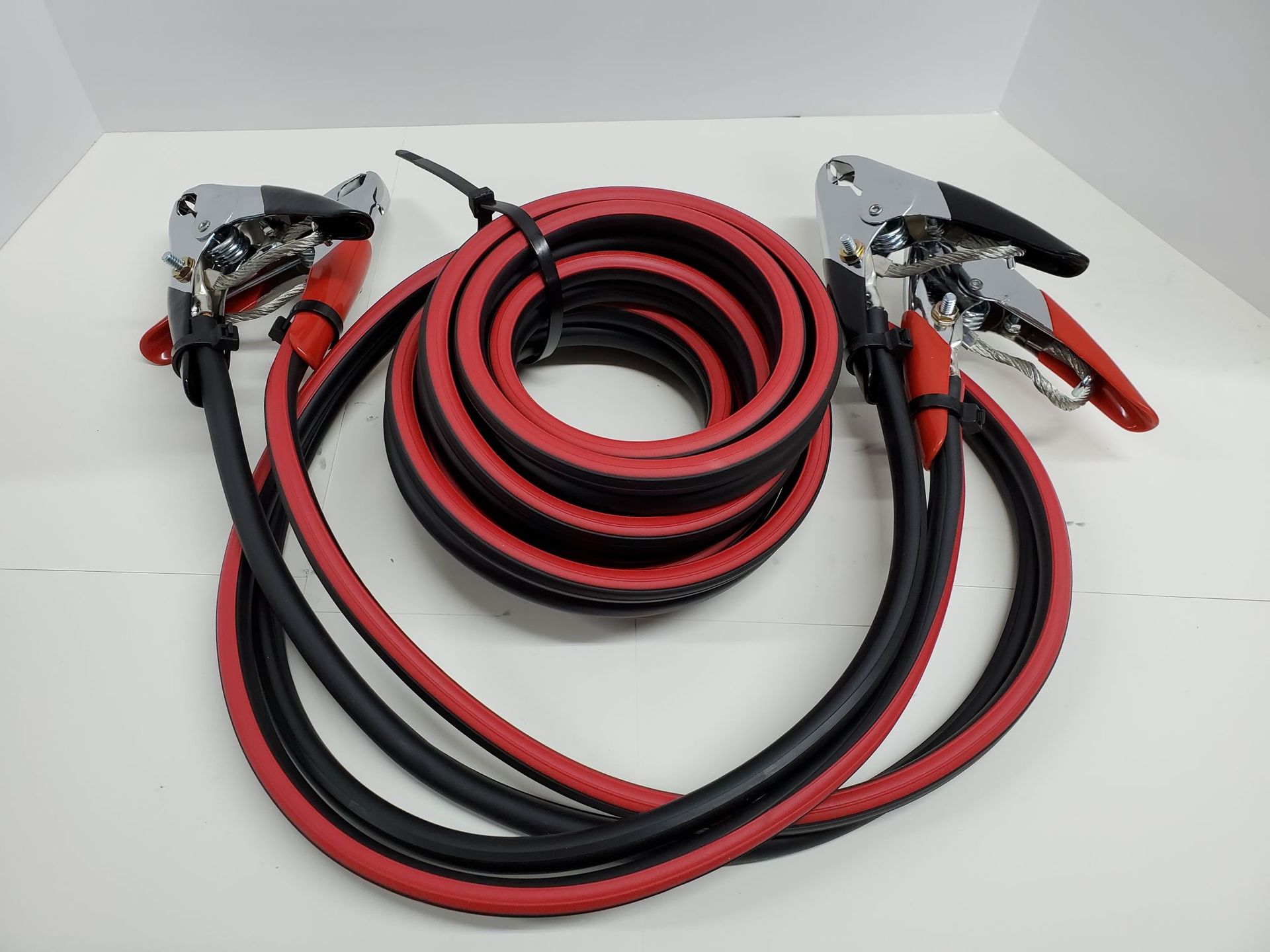 Coiled red and black jumper cables with clamps on both ends on a white background
