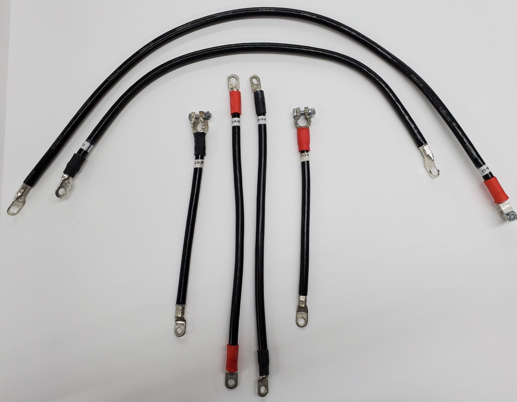 Five black cable harnesses with metal connectors, including red and white ends, laid on a light surface.