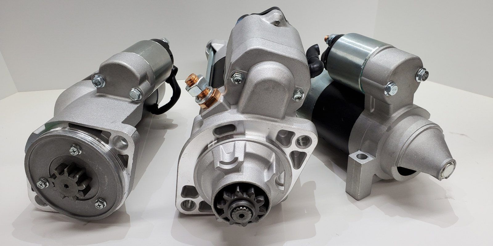 Two metal starter motors on a workbench, with tools and car parts in the background