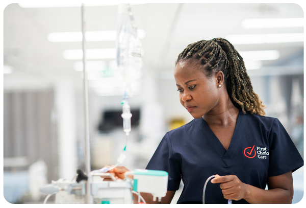 Nurse in blue scrubs checks IV drip in a hospital setting.