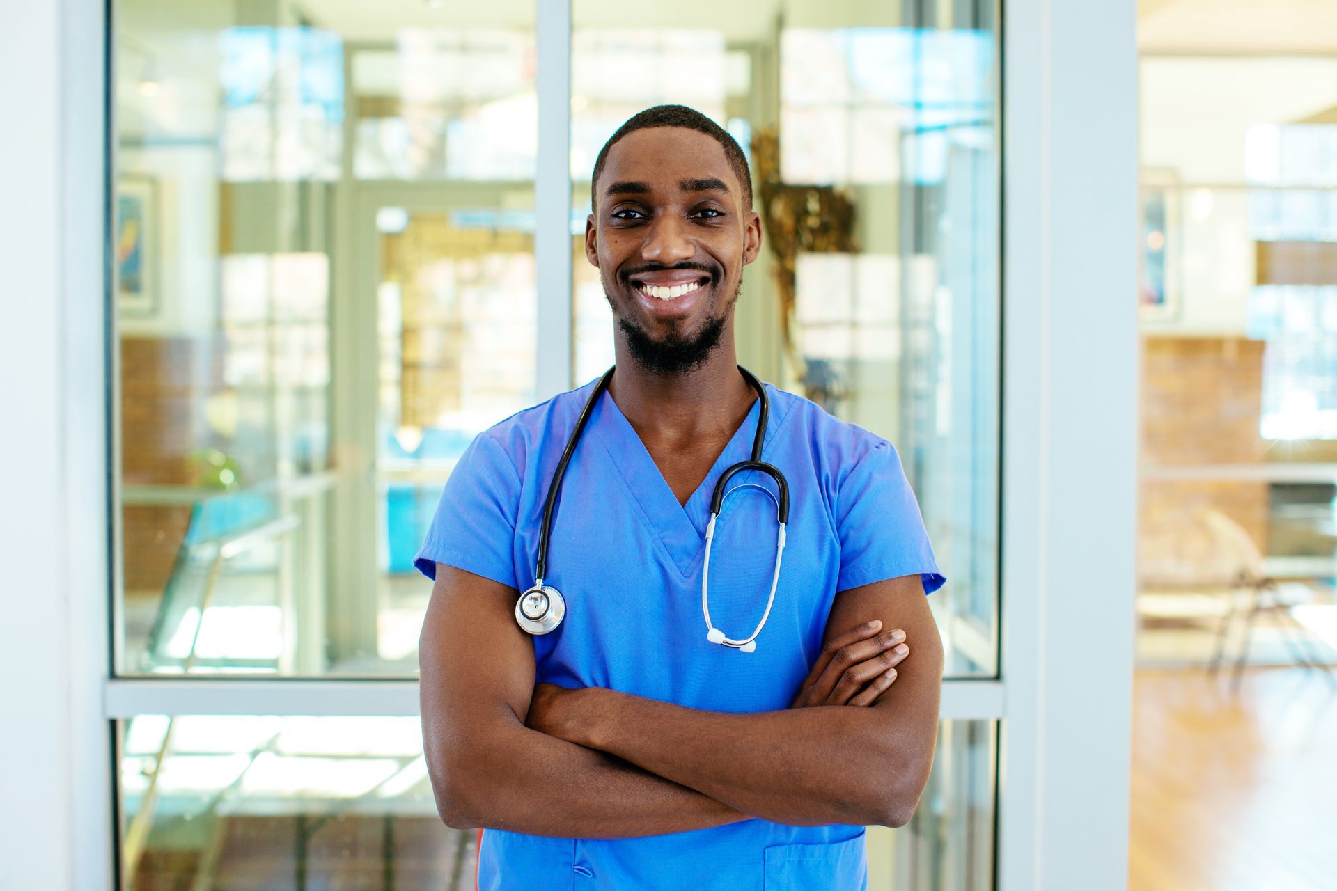 Smiling Black healthcare professional in blue scrubs with arms crossed.