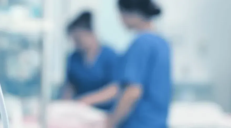 Two nurses in blue scrubs, blurred background, possibly in a hospital setting.