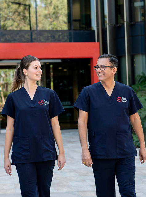 Two healthcare workers in navy scrubs walking together outside a modern building