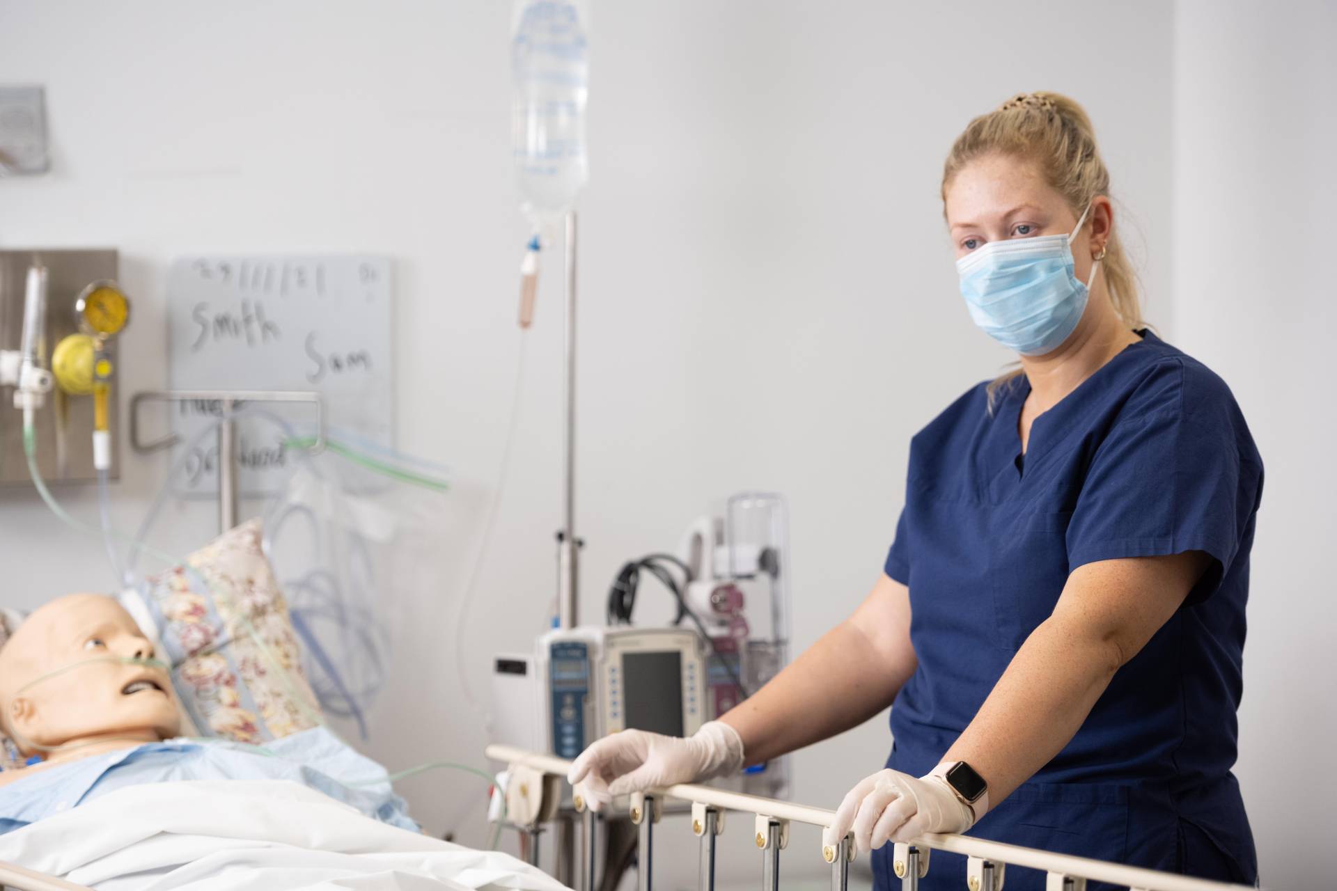 A nurse wearing a mask is standing next to a patient in a hospital bed.