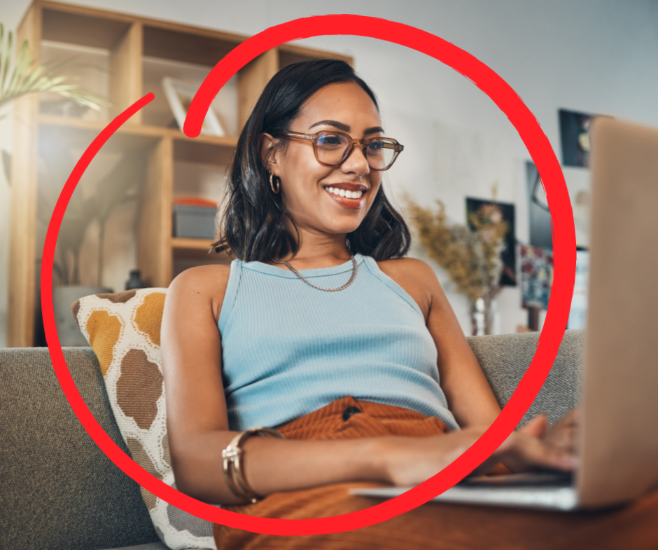 Woman wearing glasses smiles while using a laptop on a couch.
