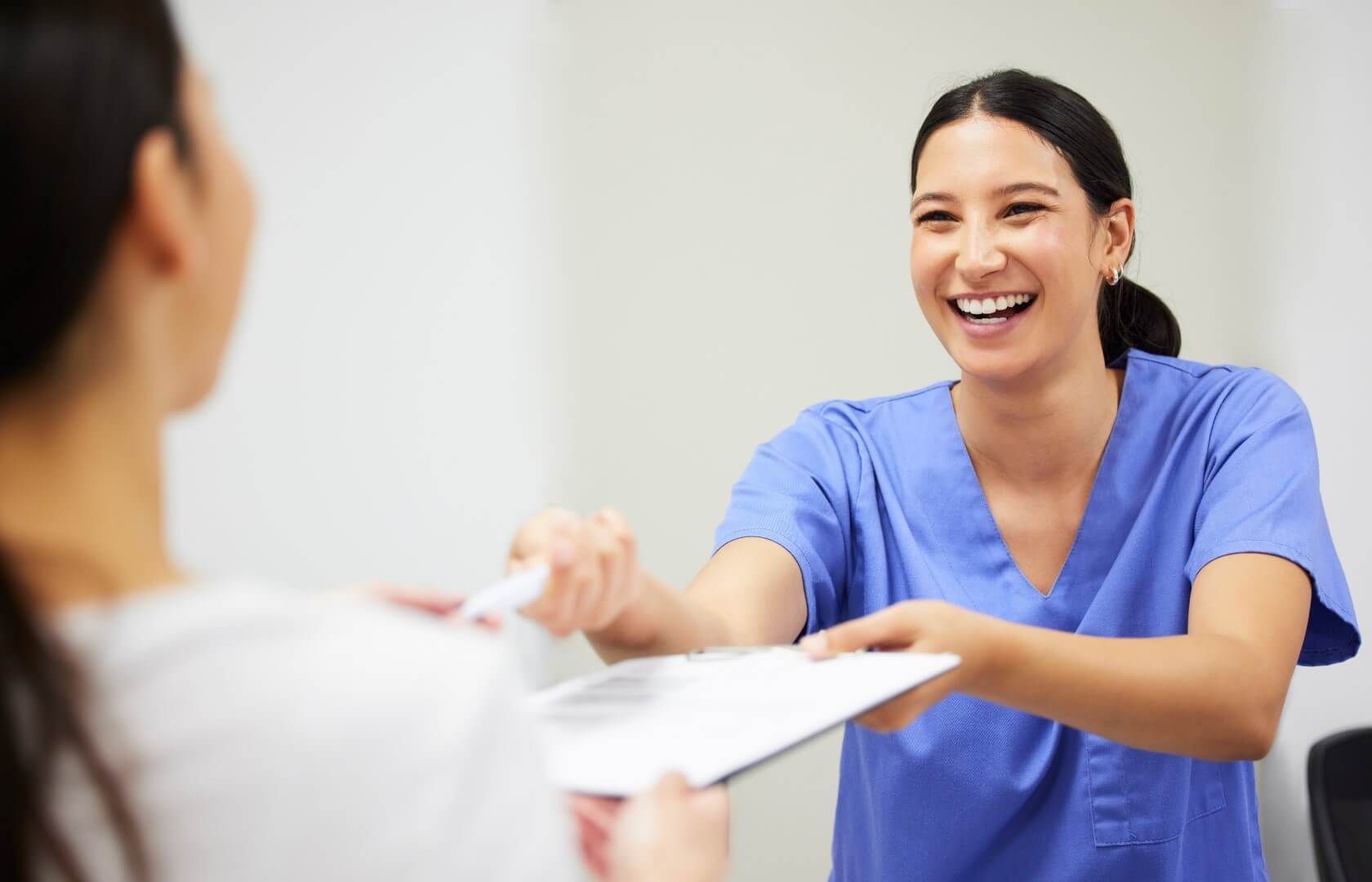 A nurse is smiling while handing a patient a clipboard.