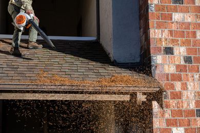 A man is using a blower to clean the roof of a brick building.