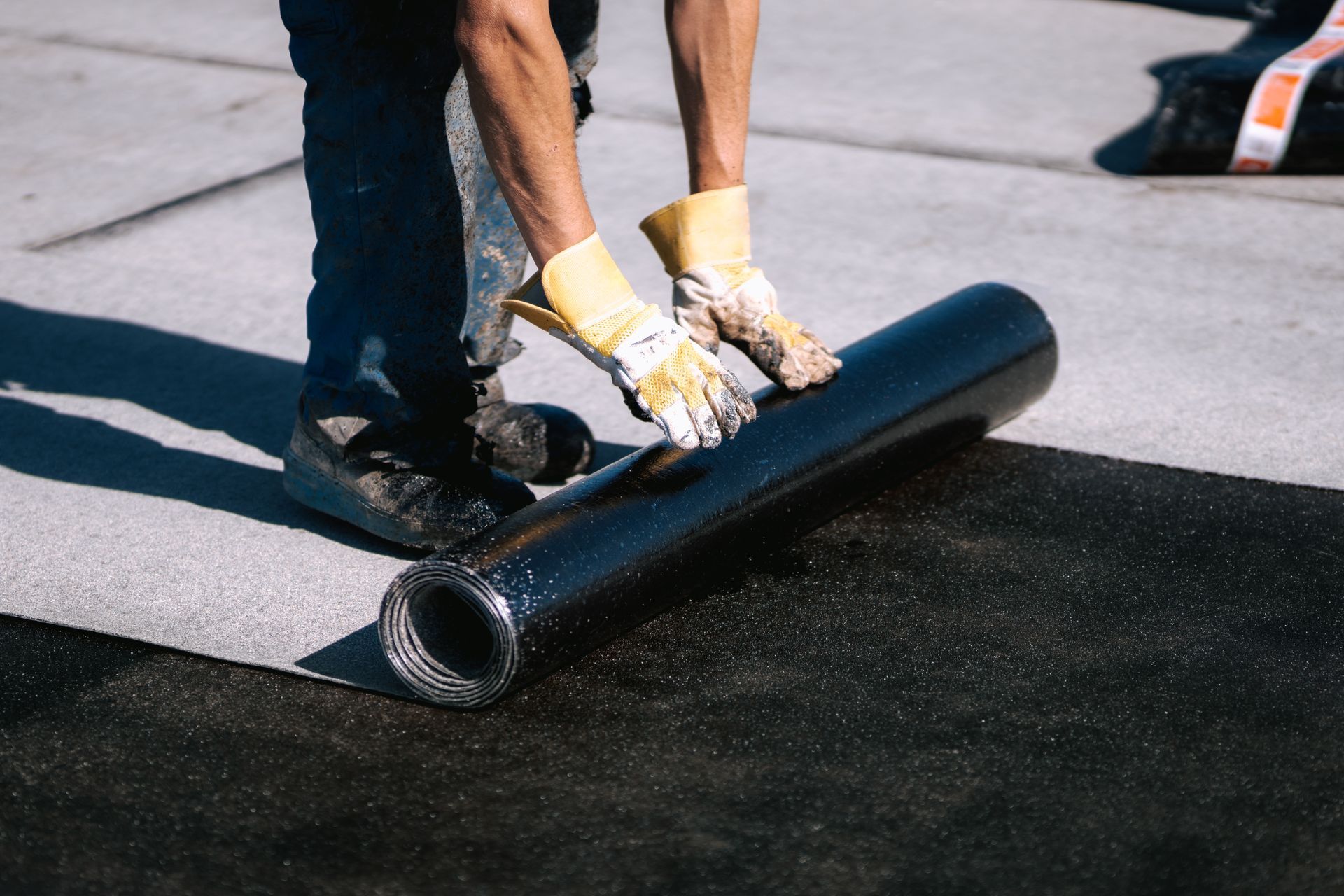 A person is rolling a roll of asphalt on a concrete surface.