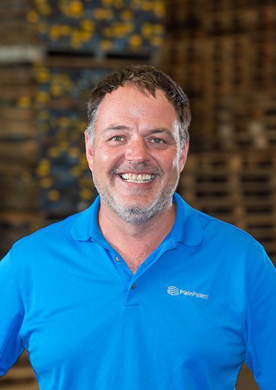 A man in a blue shirt is smiling for the camera in a warehouse. A man in a blue shirt is smiling for the camera in a warehouse.