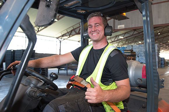 A man is driving a forklift in a warehouse and giving a thumbs up. A man is driving a forklift in a warehouse and giving a thumbs up.