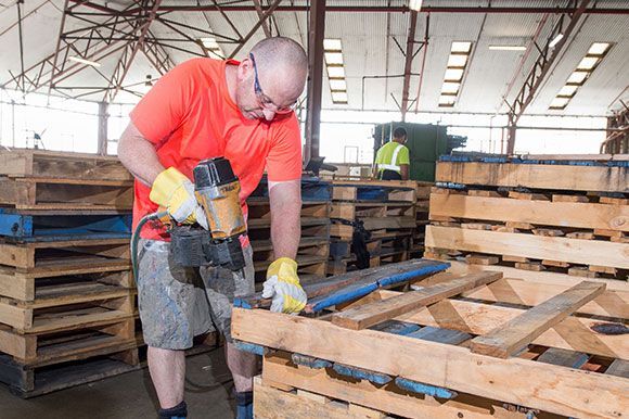 A man is working on a wooden pallet in a factory. A man is working on a wooden pallet in a factory.