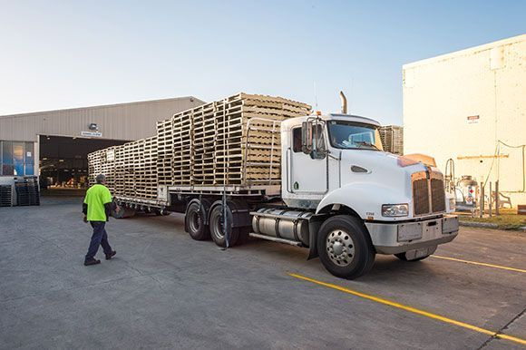 A man is walking next to a semi truck loaded with wooden pallets.