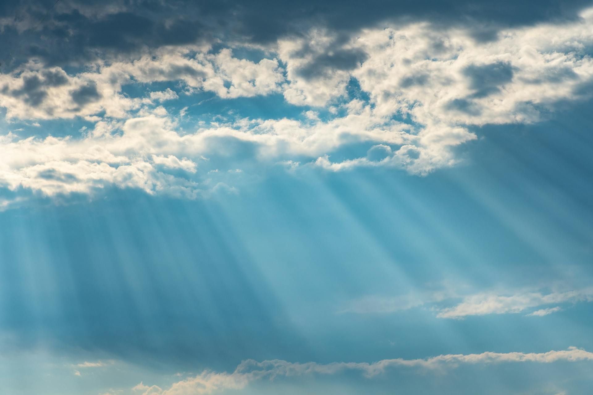 Sunlight streams through clouds in a blue sky.