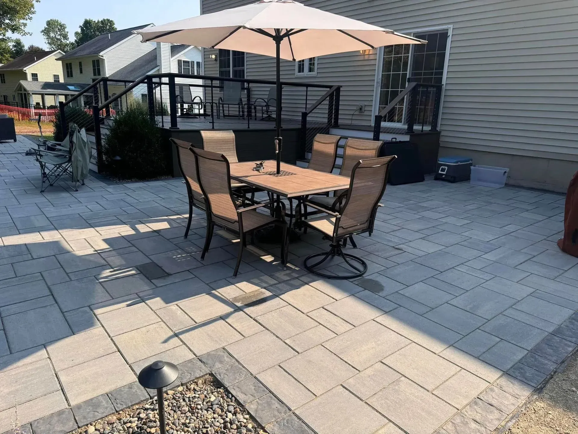 Patio with four chairs around a table under a beige umbrella on a stone paver deck
