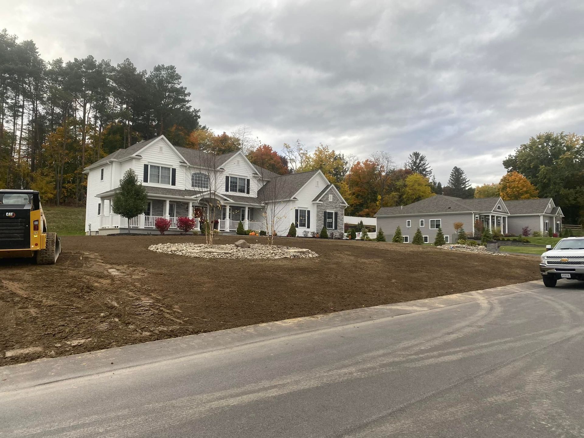 A large white house is sitting on top of a dirt field next to a road.