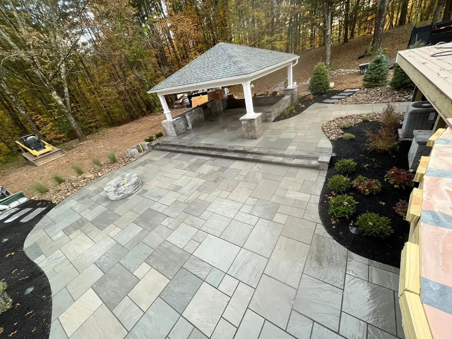 Backyard patio with gray stone pavers, a covered grill pavilion, and landscaped stone planters.