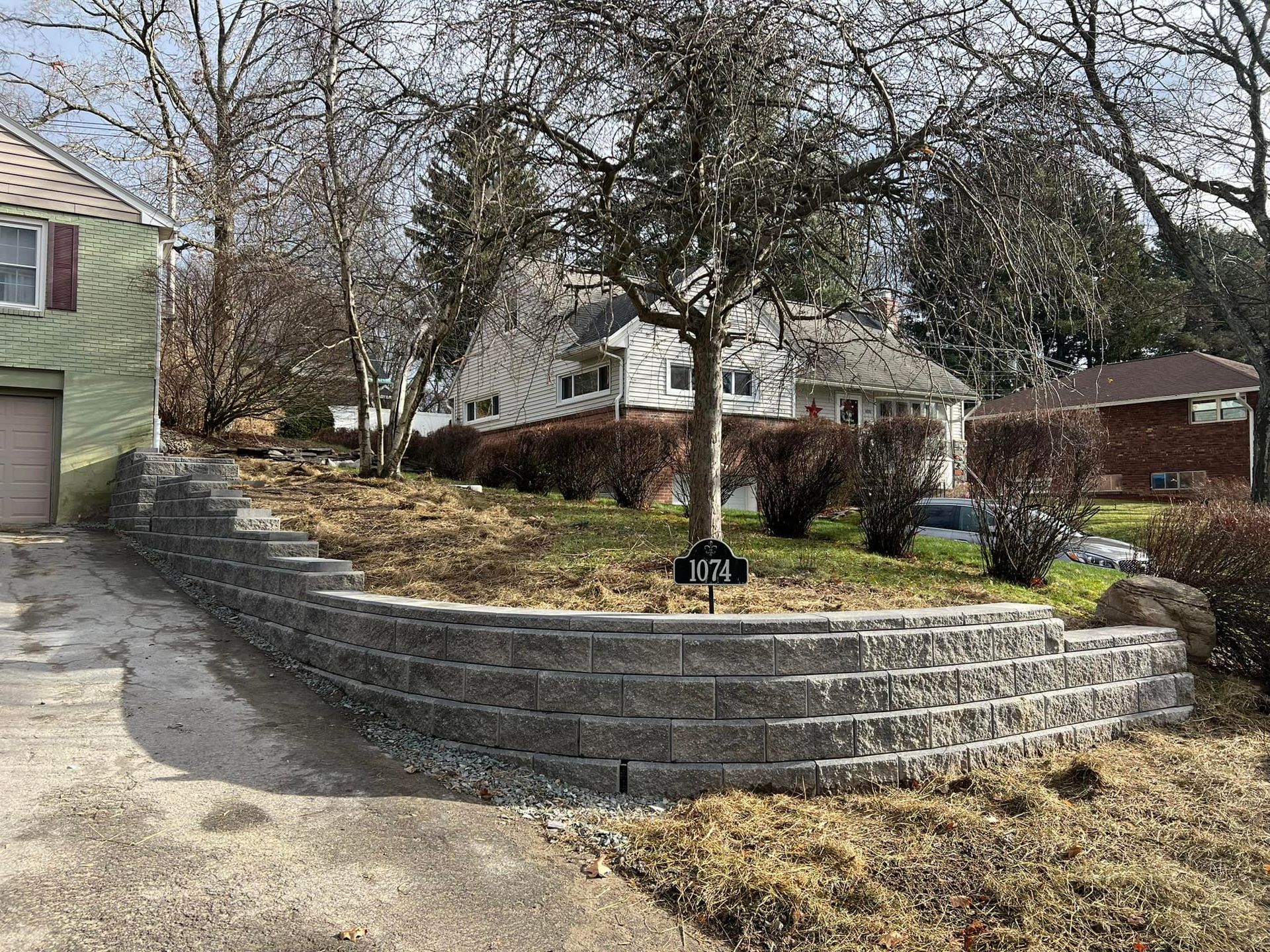 A brick wall is surrounded by grass and trees in front of a house.