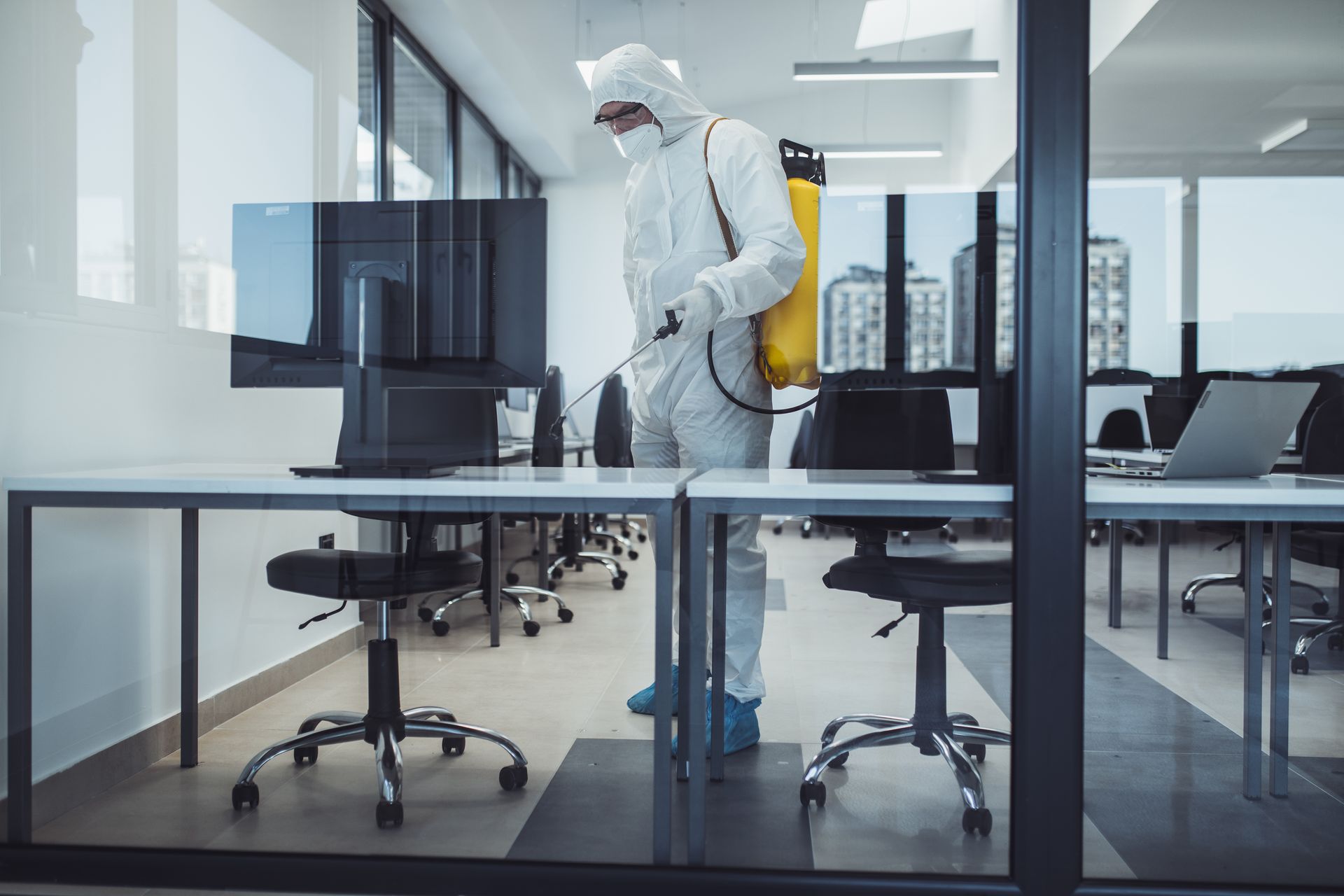 A man in a protective suit is disinfecting an office with a sprayer.
