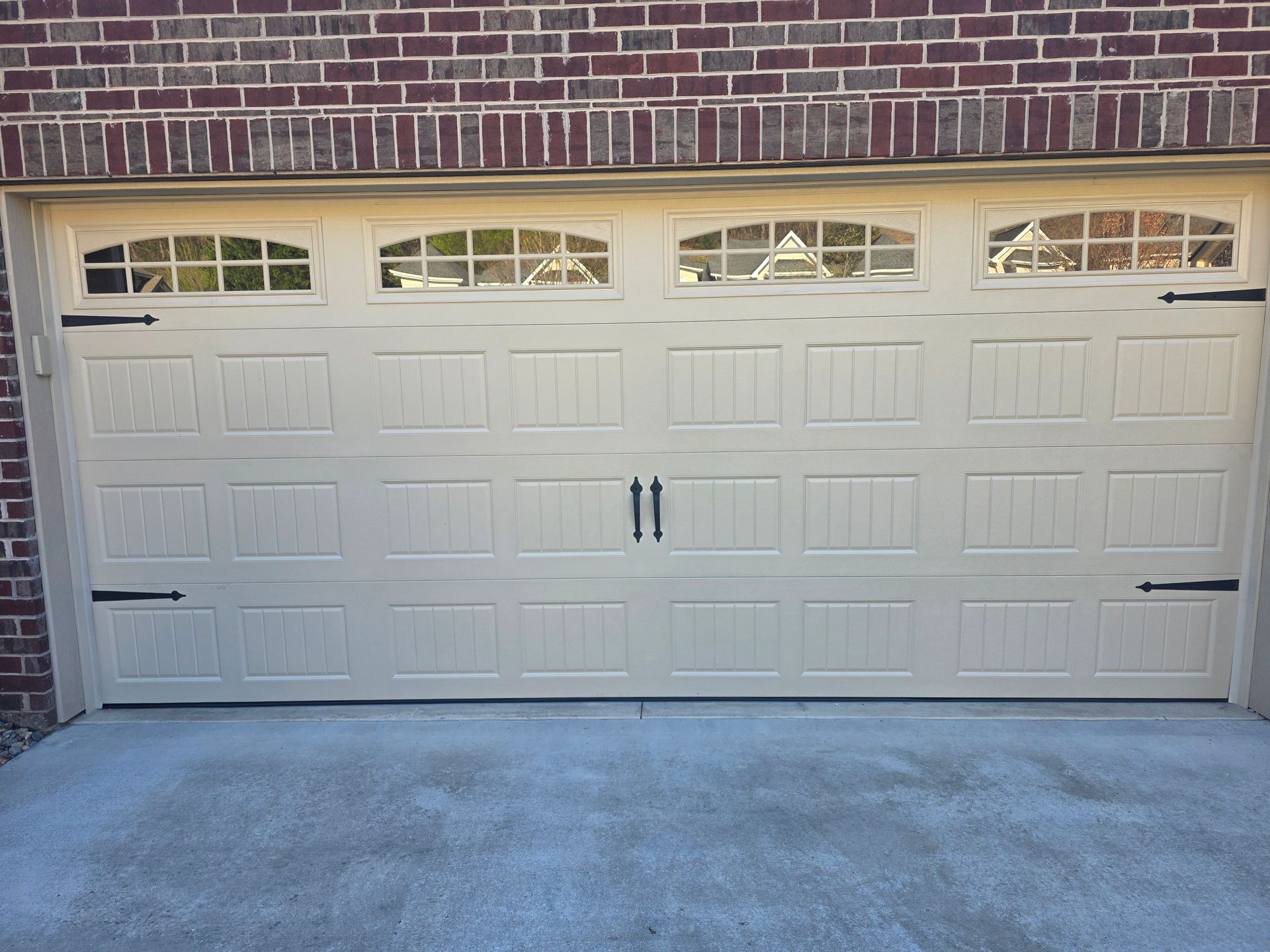 White double garage door with small window panes and brick trim above a concrete driveway