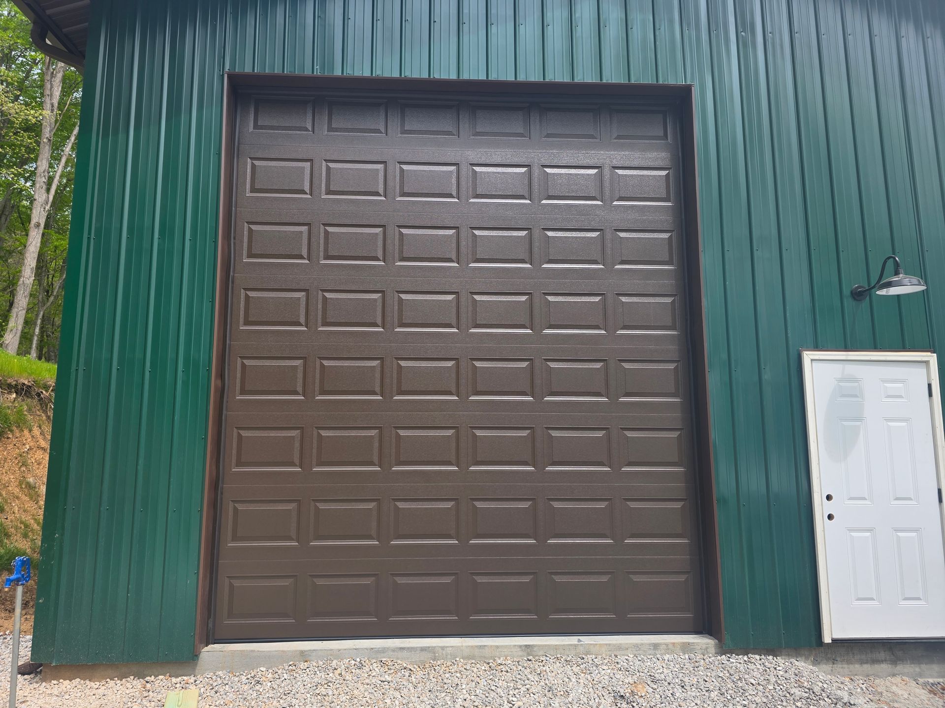Large brown garage-style door on a green building exterior, with a white side door beside it.