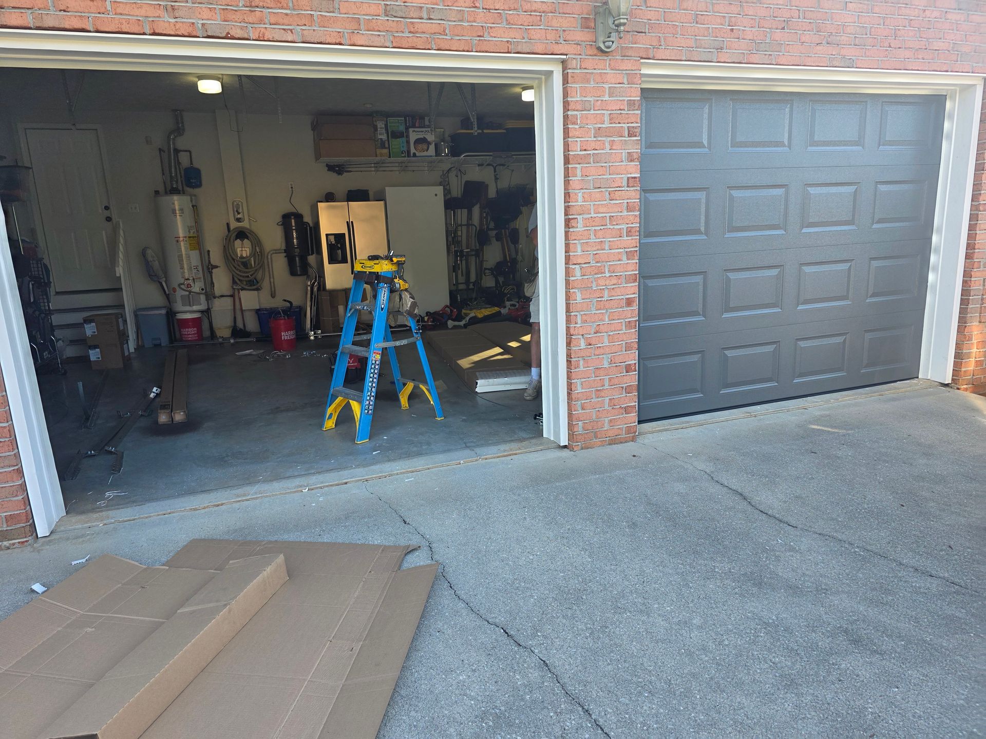 Open garage with tools and a blue step ladder; closed gray garage door beside it.