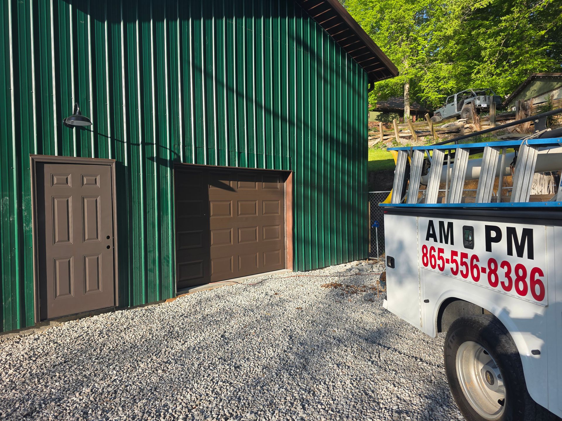 Green metal building with two brown doors beside a white AM PM truck in a gravel yard
