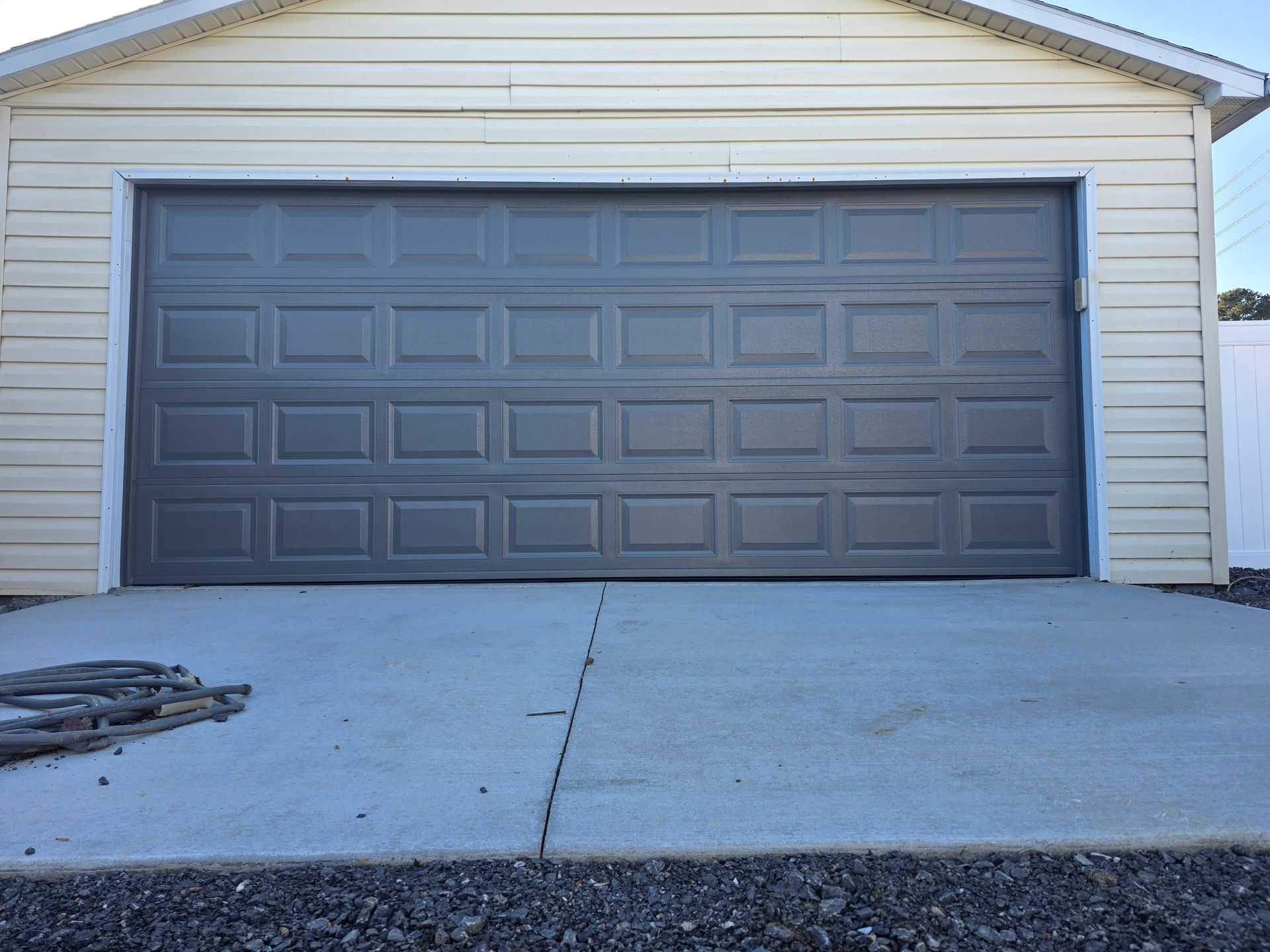 Closed gray garage door on a white-sided house with a concrete driveway in front
