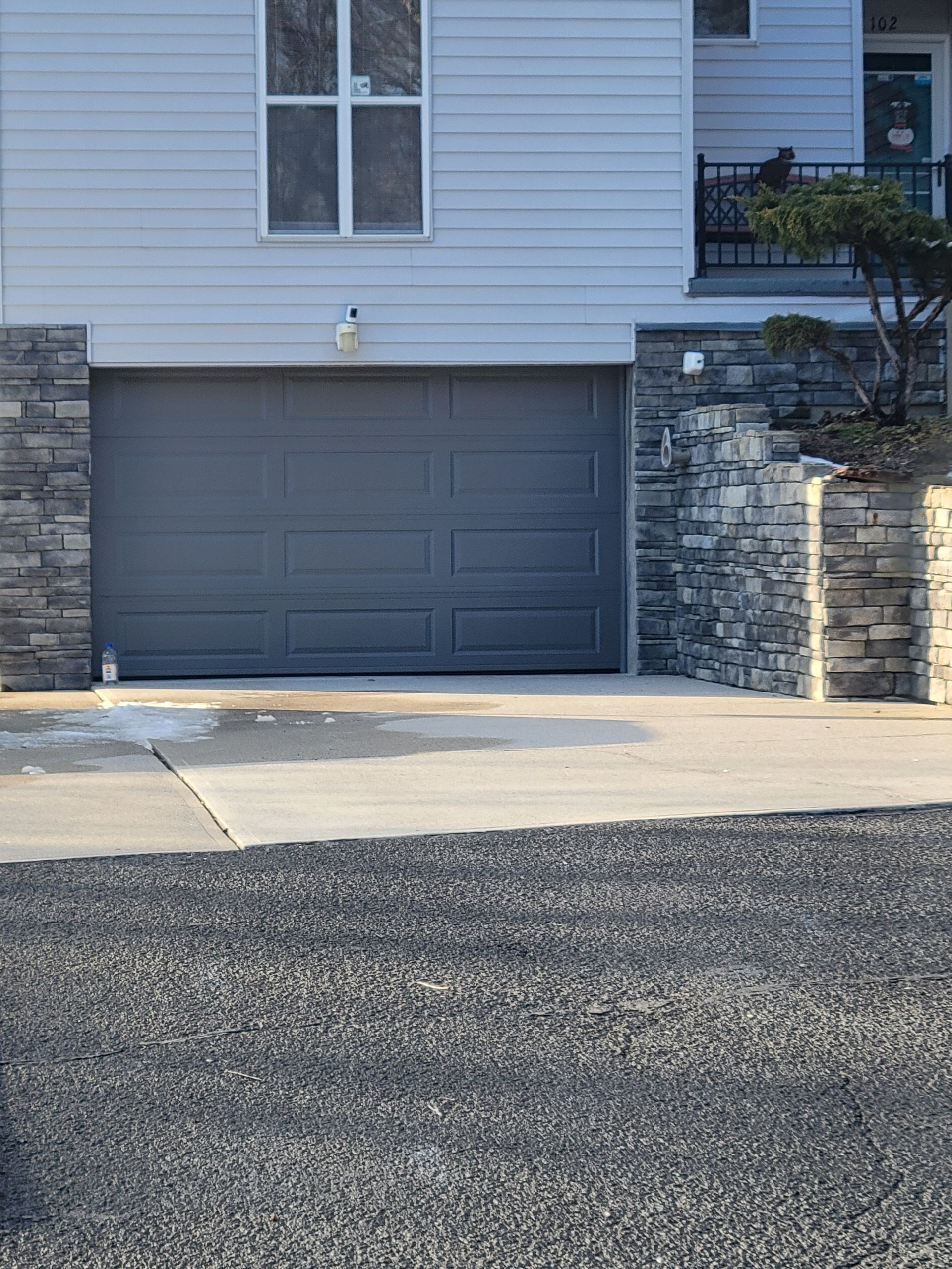 Gray garage door with stone columns and concrete driveway.
