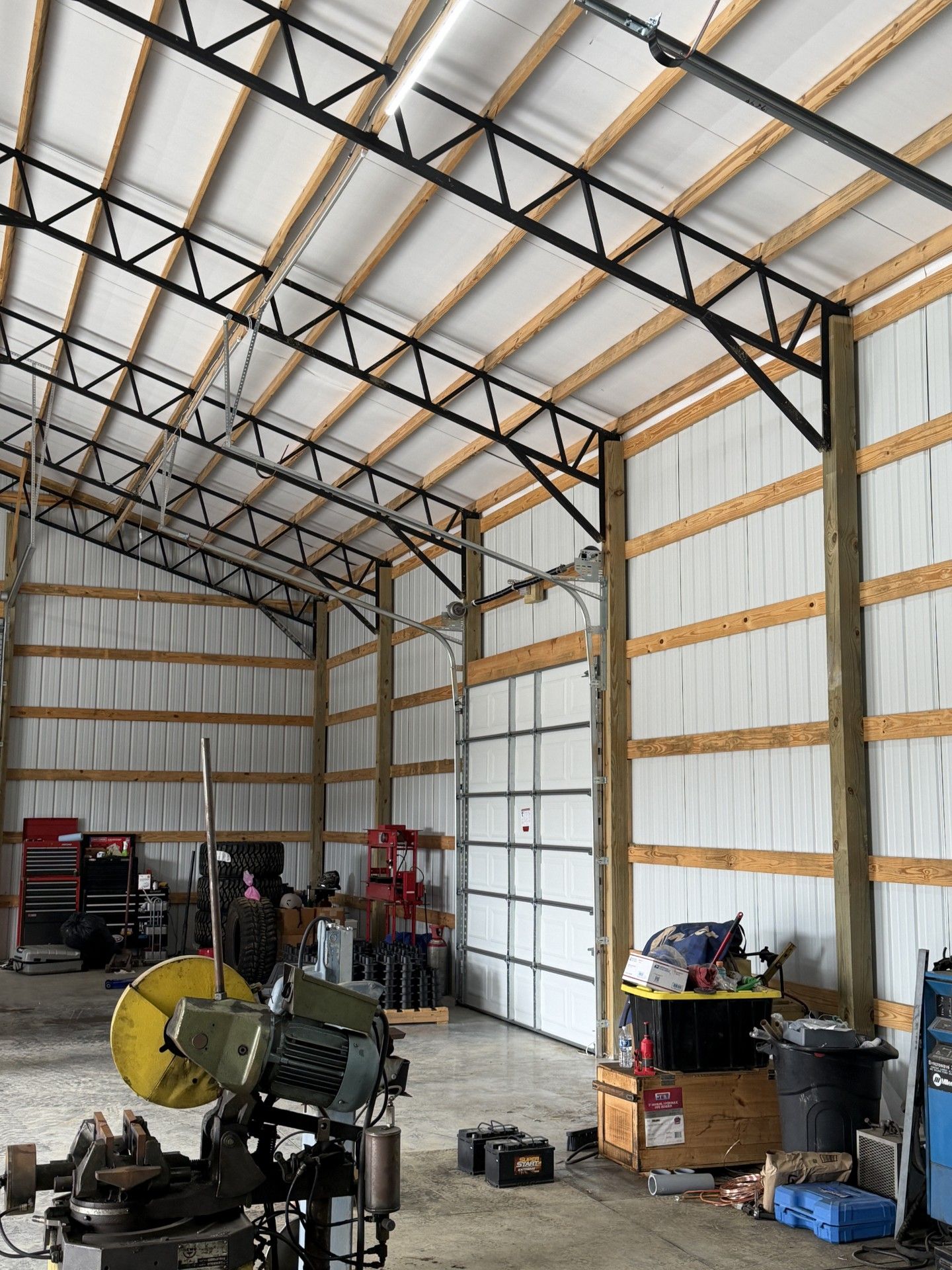 Large unfinished metal workshop with exposed trusses, equipment, shelves, and tools along the walls
