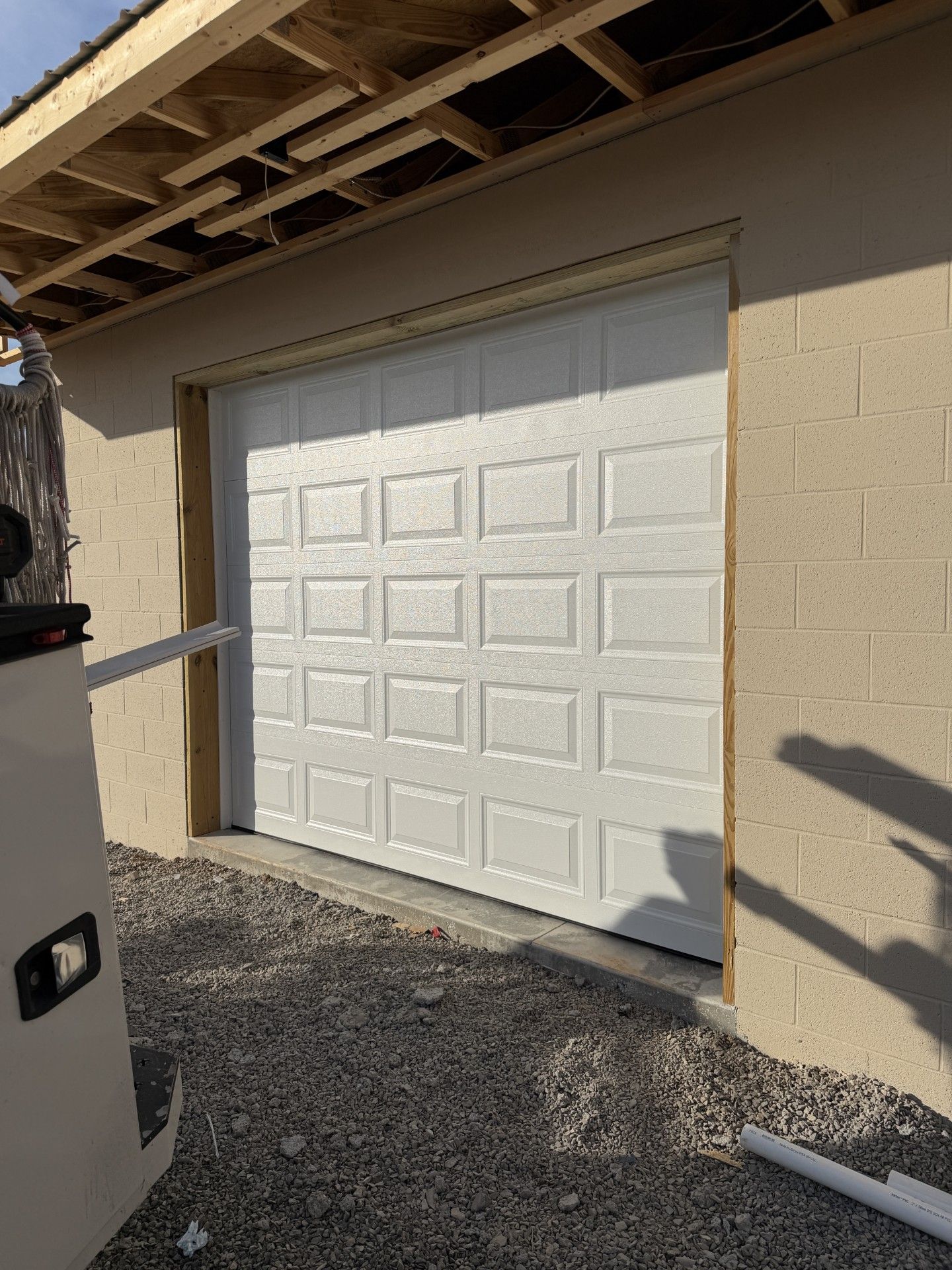 White garage door on a beige stucco house under a roof overhang, with gravel driveway in front.