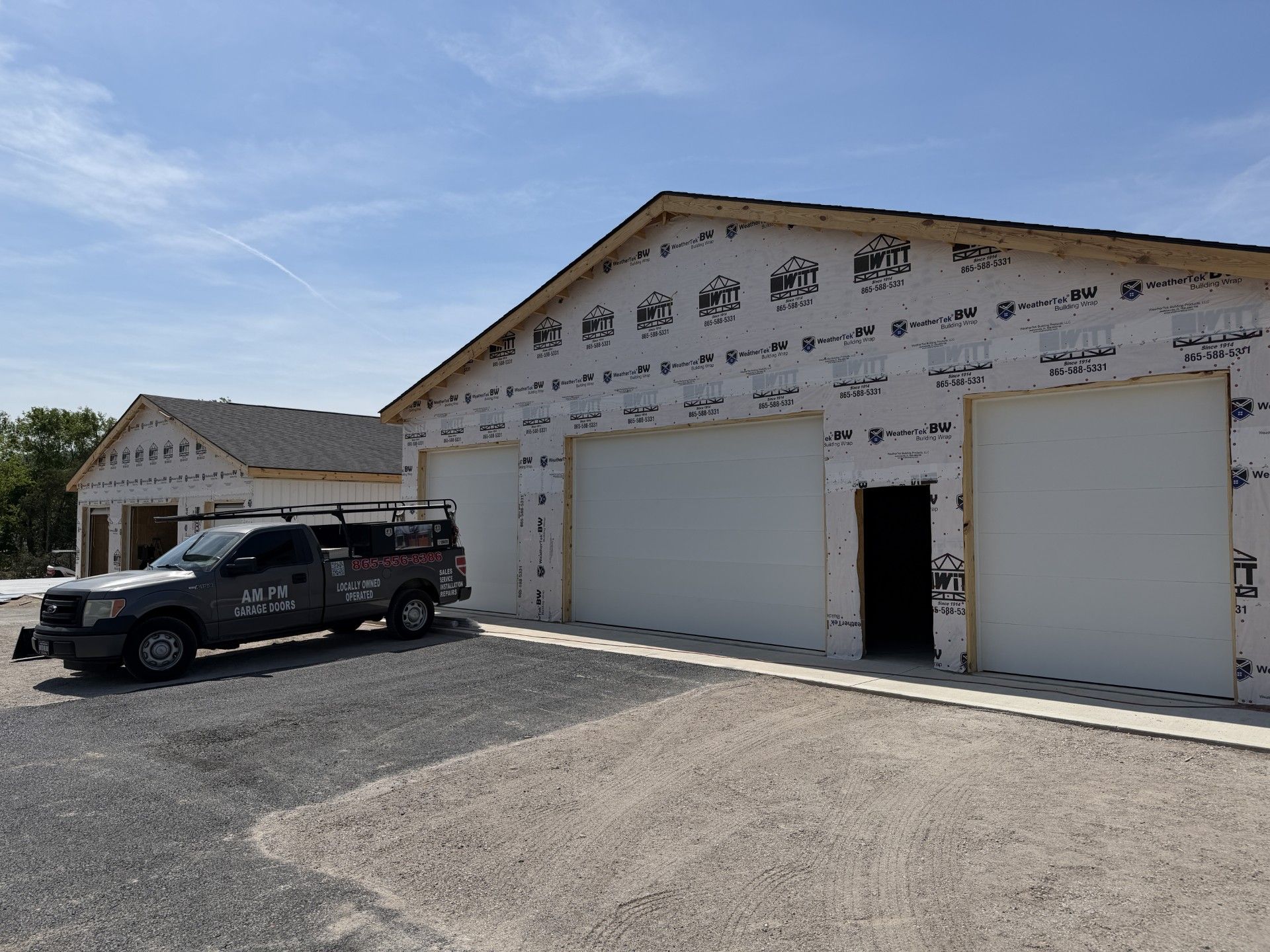 Black SUV parked outside a white auto repair garage with three large bay doors under a blue sky