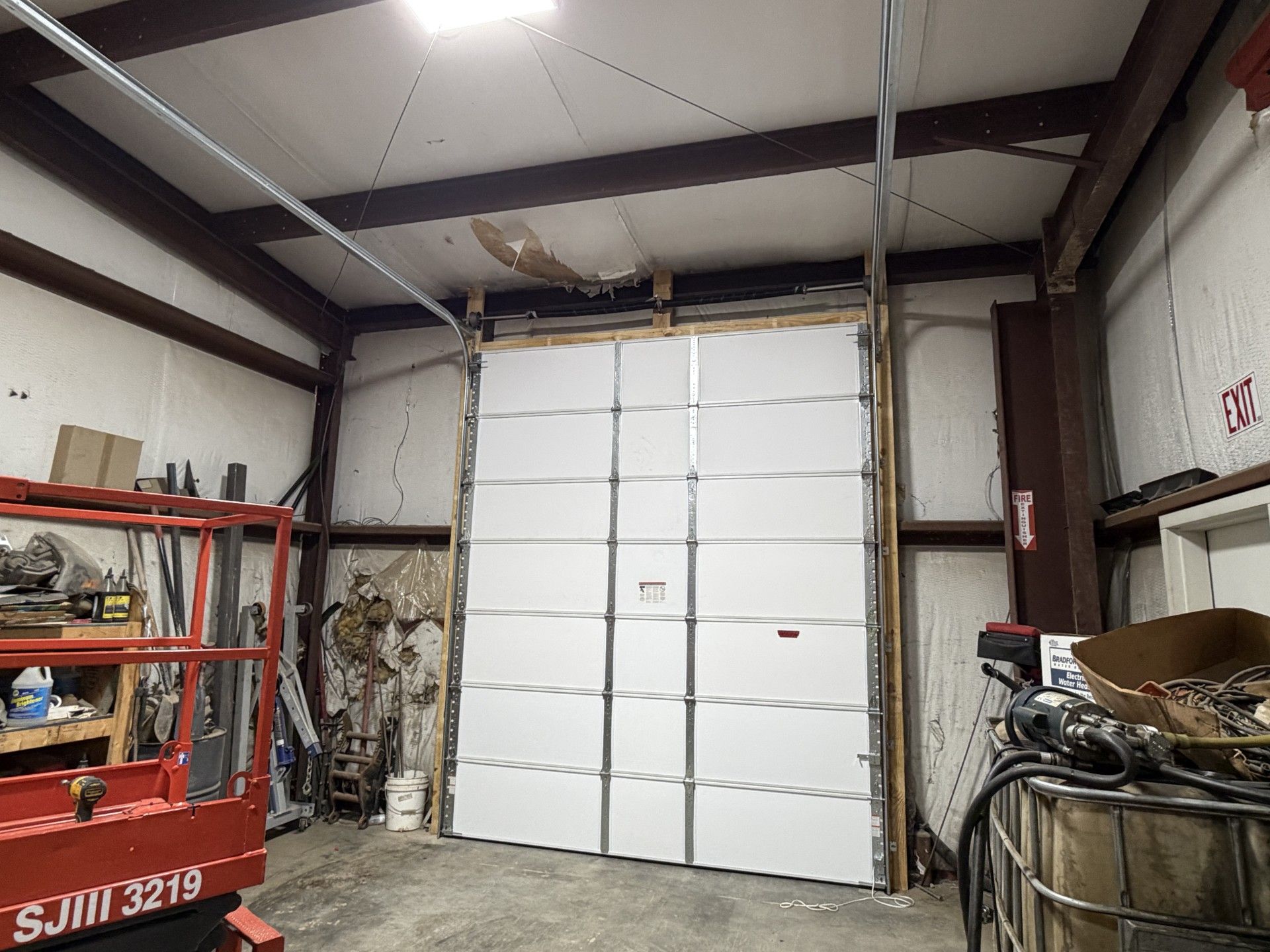 Industrial garage with a large white roll-up door, metal shelving, and a red lift in the foreground