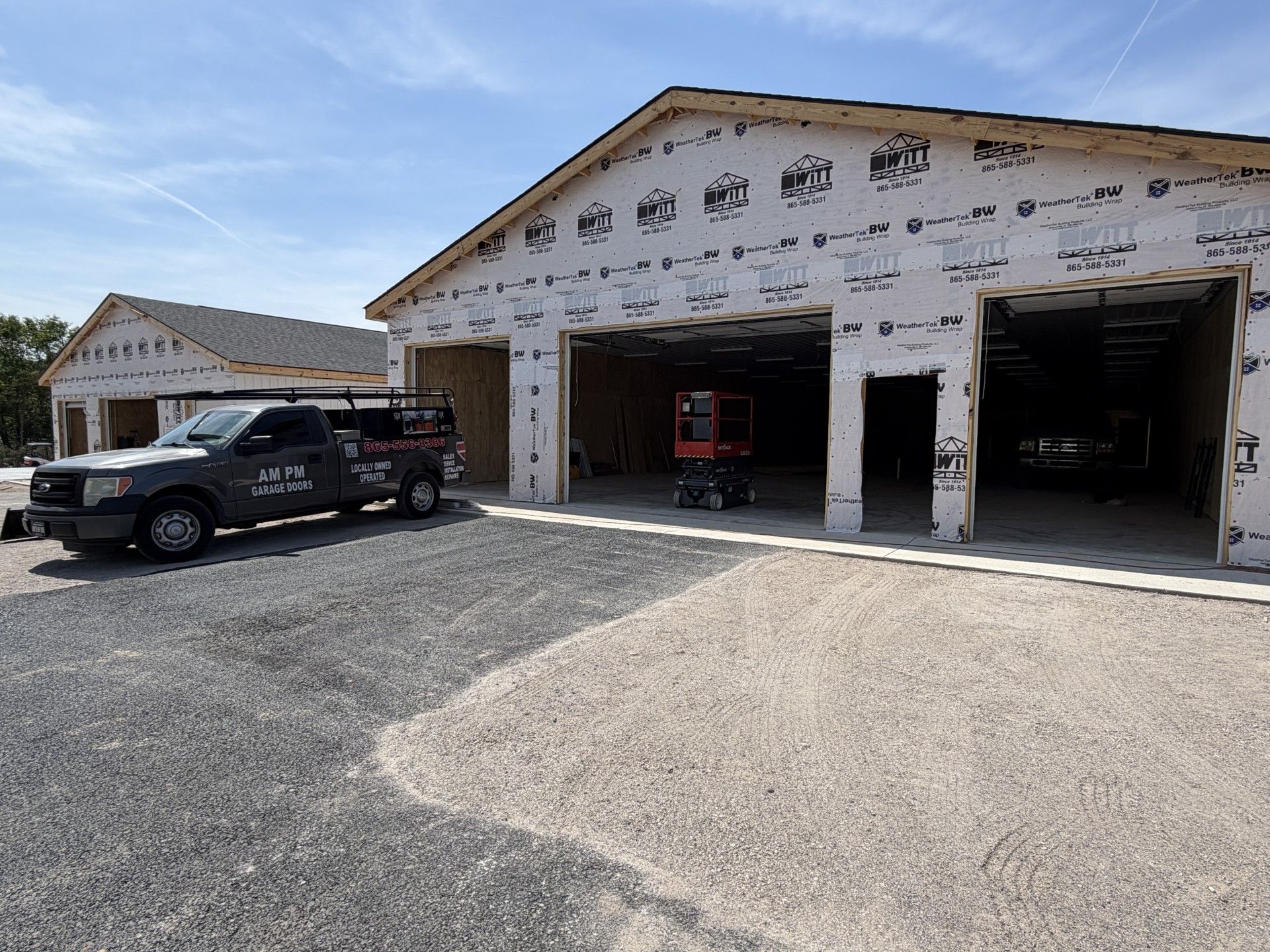 Black pickup truck outside unfinished garage bays under construction on a sunny day