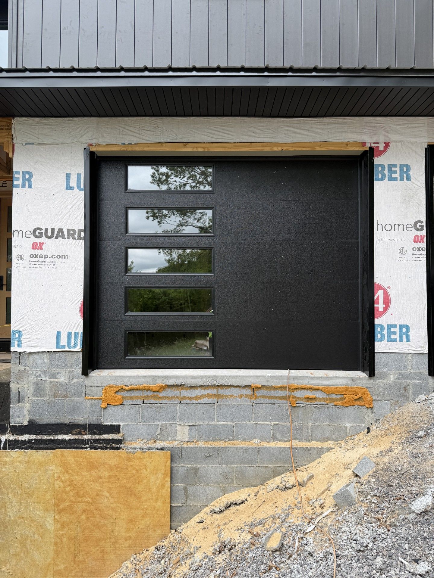 Black modern garage door with narrow horizontal windows in a construction opening with insulation around it