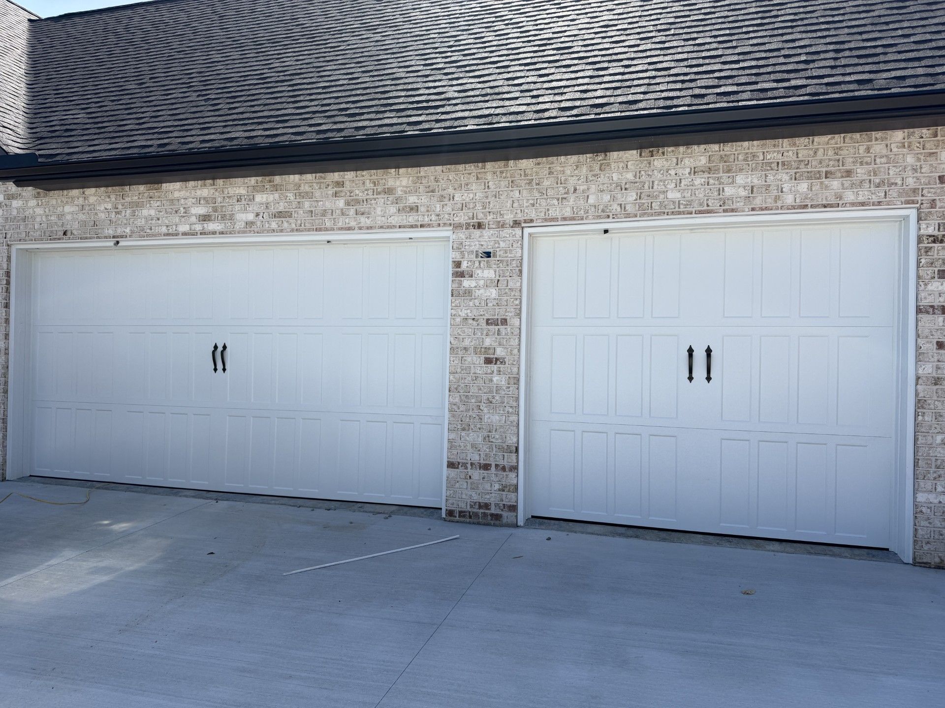 Two white garage doors in a stone-and-shingle exterior wall beside a driveway.